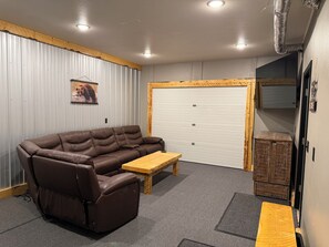 A room with a brown leather sofa, a wooden coffee table, a grey carpet, a white garage door, and a wooden cabinet. - Spacious 3-bedroom 2 living apartment with Alaska theme. TV’s in every room. (North Pole)