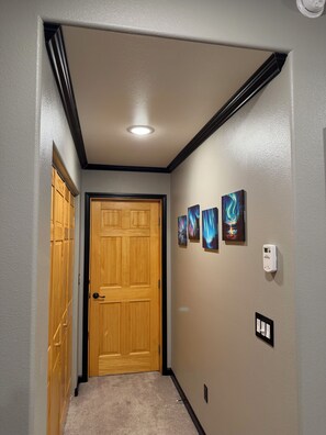 A hallway with a wooden door, a wall-mounted thermostat, and three framed pictures. - Spacious 3-bedroom 2 living apartment with Alaska theme. TV’s in every room. (North Pole)