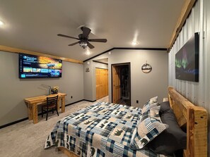 A bedroom with a bed, a desk, a ceiling fan, a TV, and a door. - Spacious 3-bedroom 2 living apartment with Alaska theme. TV’s in every room. (North Pole)