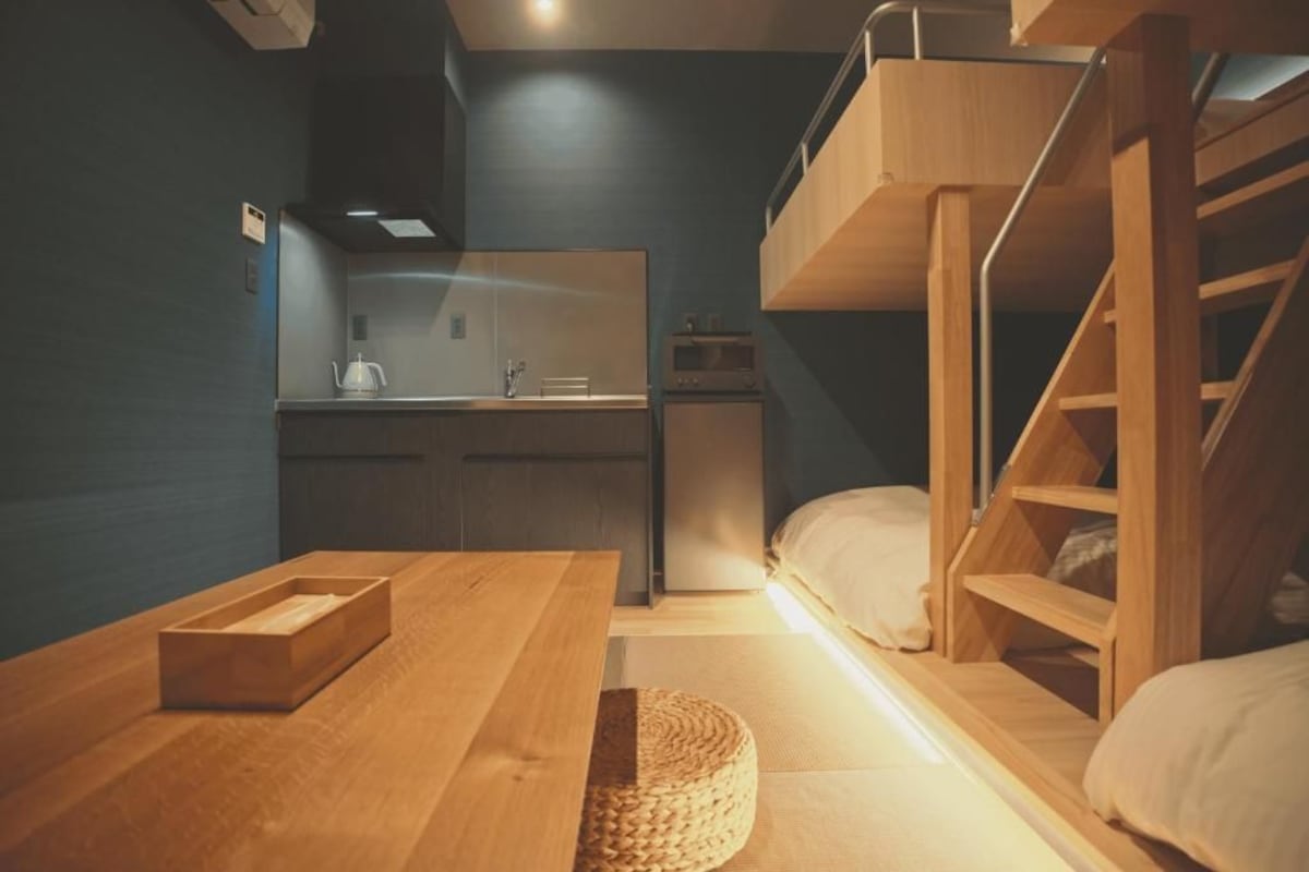 Een kleine kamer met een stapelbed, een kitchenette en een houten tafel.