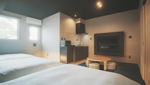 A modern hotel room with two beds, a kitchenette, a flat-screen TV, and a small dining table. - Amu  (Beppu)