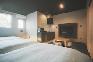 Een moderne hotelkamer met twee bedden, een kitchenette, een flatscreen televisie en een eettafeltje.