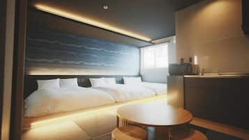 A modern hotel room with a large bed, a dining table, and a kitchen area.