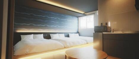 A modern hotel room with a large bed, a dining table, and a kitchen area.