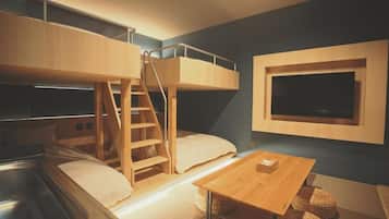 Habitación con literas, una escalera de madera, un televisor en la pared y una pequeña mesa de madera.