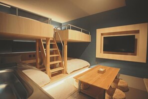 Ein Schlafraum mit Etagenbetten, einer Holzleiter, einem an der Wand befestigten Fernseher und einem kleinen Holztisch.