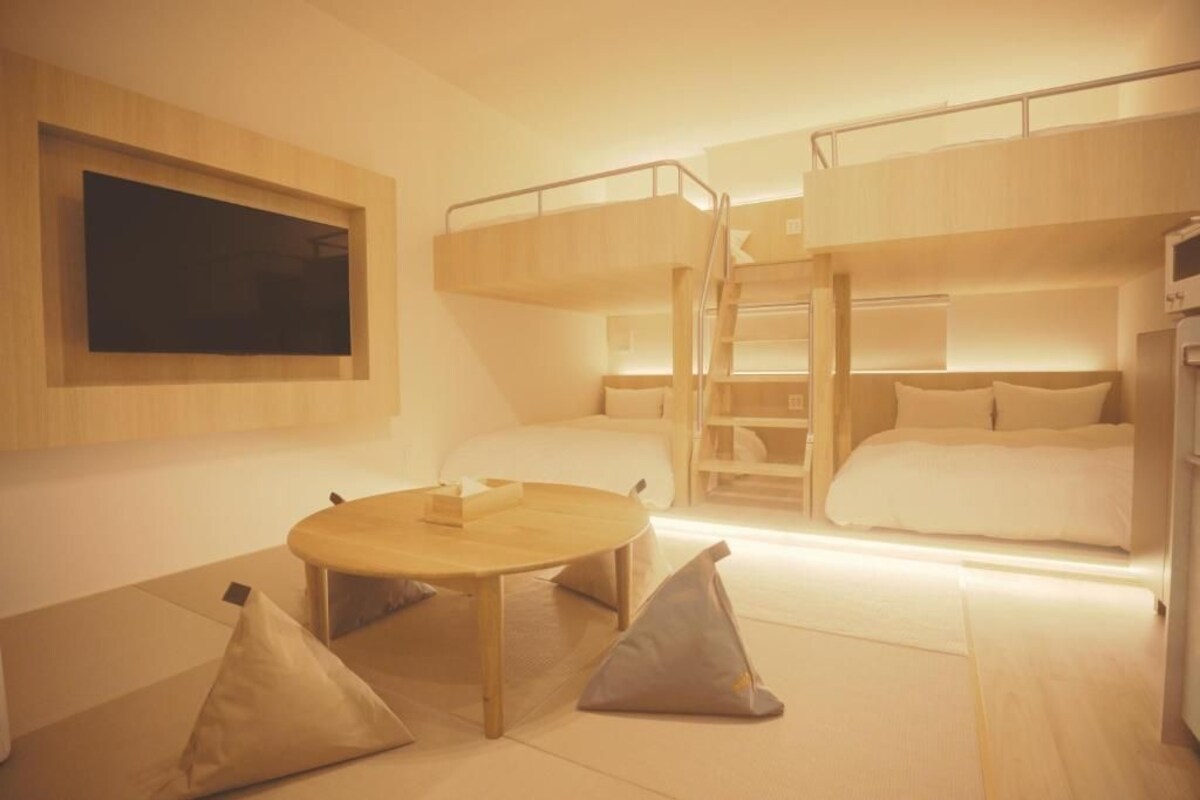 Een slaapkamer met een stapelbed, een televisie, een ronde tafel en kussens op de vloer.