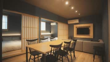 A modern hotel room with a dining area, a sofa, a TV, and a sliding door.