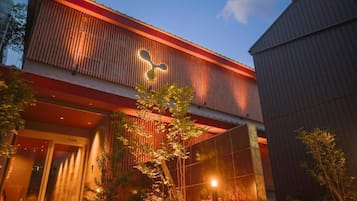 A building with a prominent logo on the facade, a glass entrance, and a well-lit outdoor area with plants.
