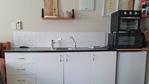 Cocina compacta con armarios blancos, pileta de acero inoxidable, microondas y heladera pequeña.