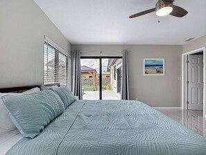 Ein Schlafzimmer mit einem Bett, einem Deckenventilator, einem Fenster mit Jalousien und einer Tür.