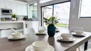 A modern dining area with a long table set for a meal, white plates, and bowls. - Northshore Waterfront Resort (Port Charlotte)