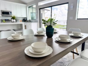 A modern dining area with a long table set for a meal, white plates, and bowls. - Northshore Waterfront Resort (Port Charlotte)