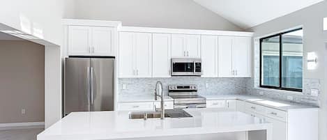 A modern kitchen with white cabinetry, stainless steel appliances, and a central island with bar stools.