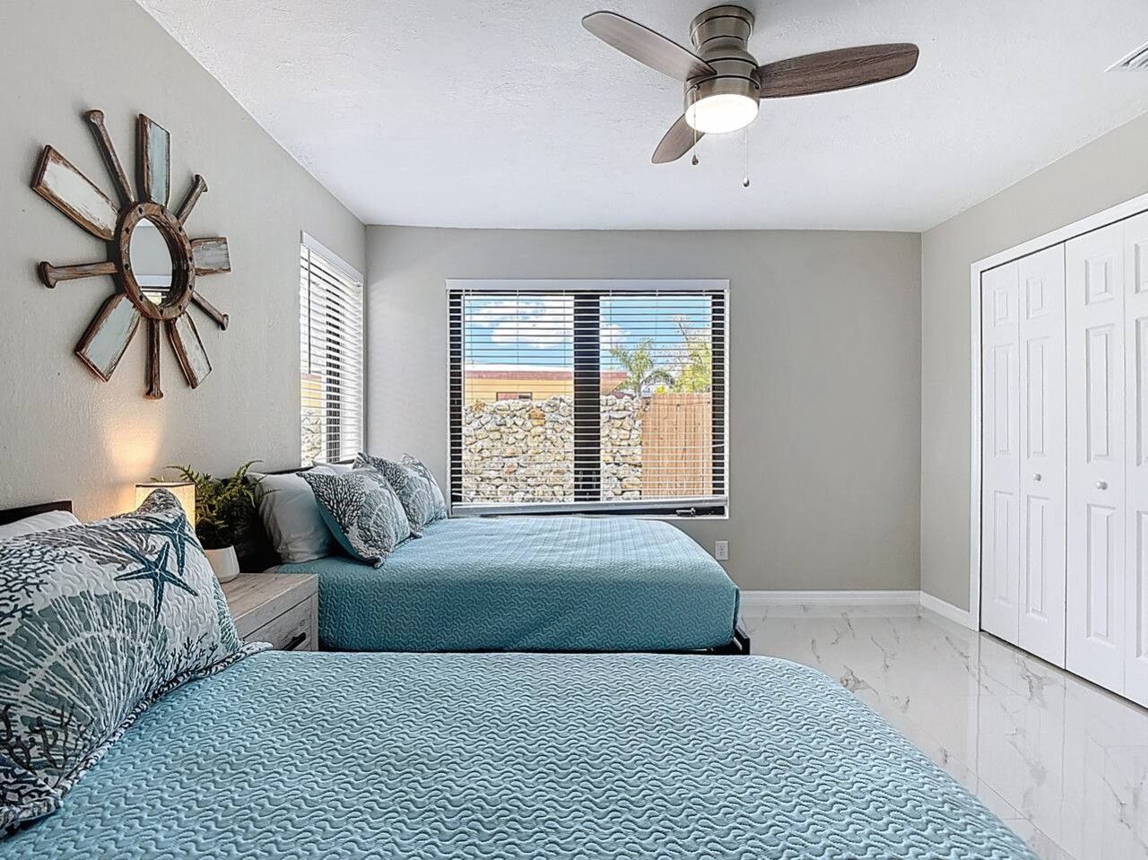 Une chambre à coucher avec un lit, un ventilateur de plafond, une fenêtre avec des stores et une porte.