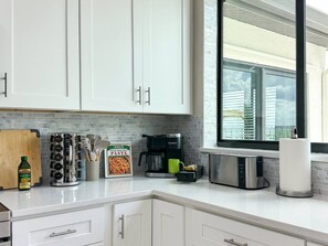 Eine moderne Küche mit weißen Schränken, einer Kaffeemaschine, einem Toaster und einem Schneidebrett.