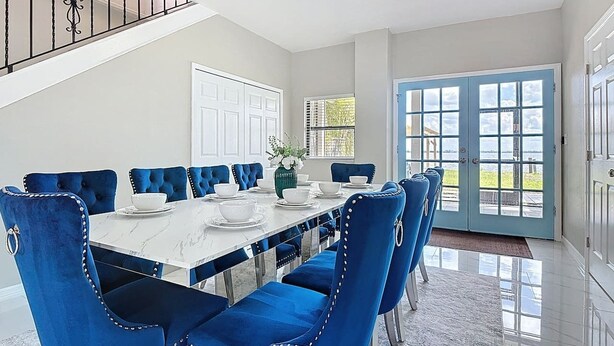 A dining area with a white marble table, blue upholstered chairs, and a view through a glass door. - Northshore Waterfront Resort (Port Charlotte)