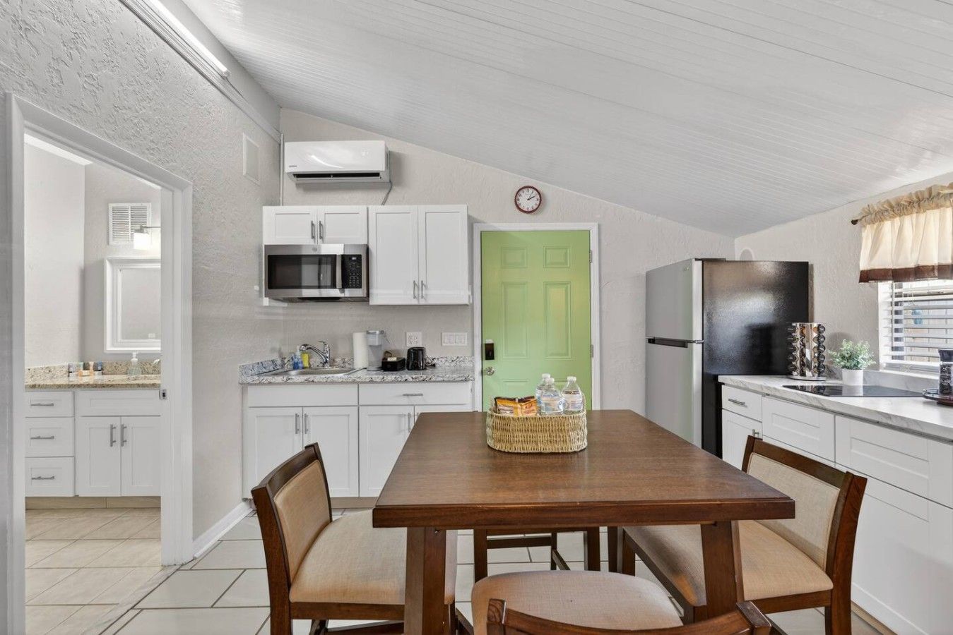 A compact kitchen with white cabinets, a microwave, a refrigerator, and a dining table with chairs.