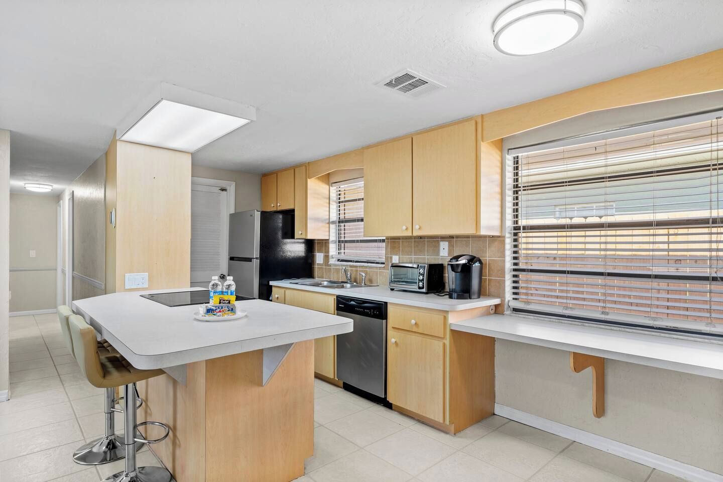 A modern kitchen with a bar area, a dishwasher, a refrigerator, and a window with blinds.