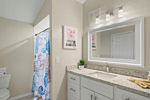A bathroom with a shower curtain, a sink, a mirror, and a framed picture on the wall. - Shark Tooth Coastal Retreat (Englewood)