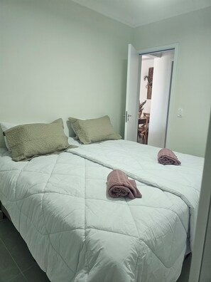 A double bed with a white duvet and two pillows, a door leading to a bathroom, and a towel on the bed. - Beautiful Luxury Resort Apartment (Guarujá)