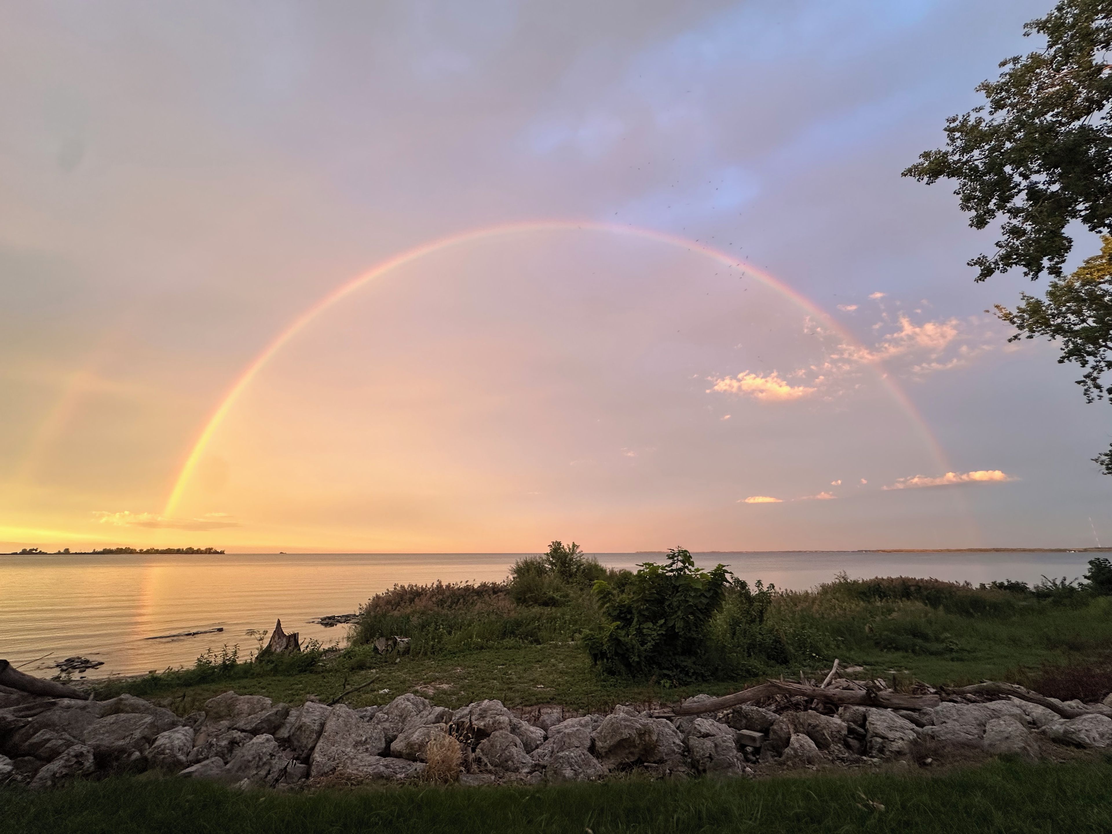 Eine natürliche Landschaft mit blauem Himmel, einem Regenbogen und einem Gewässer.