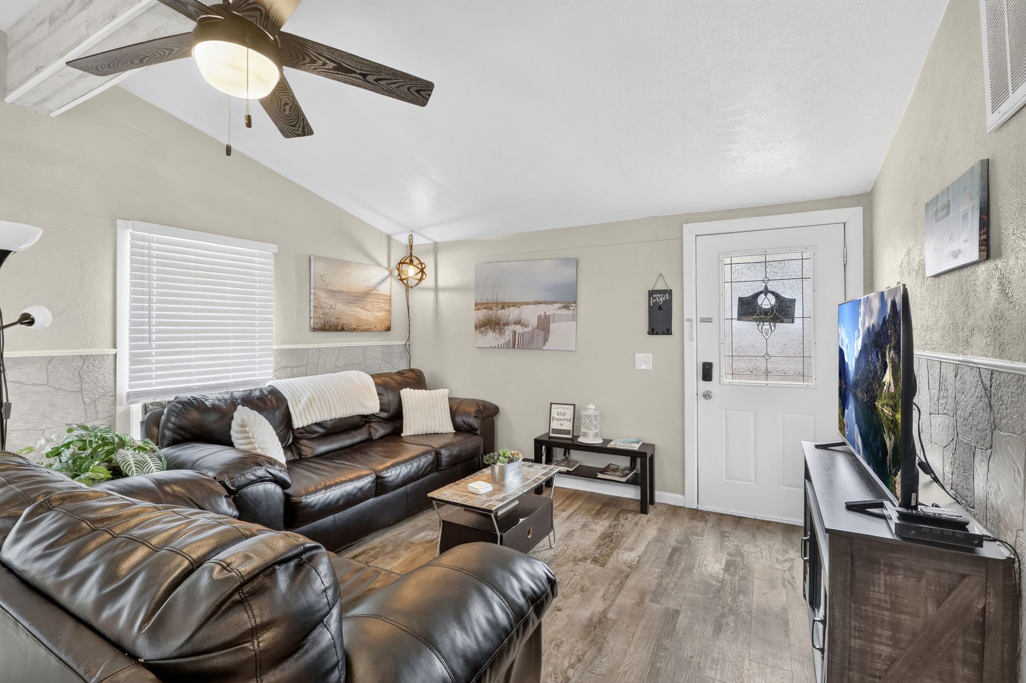 A living room with a leather sofa, a coffee table, a ceiling fan, and a television.