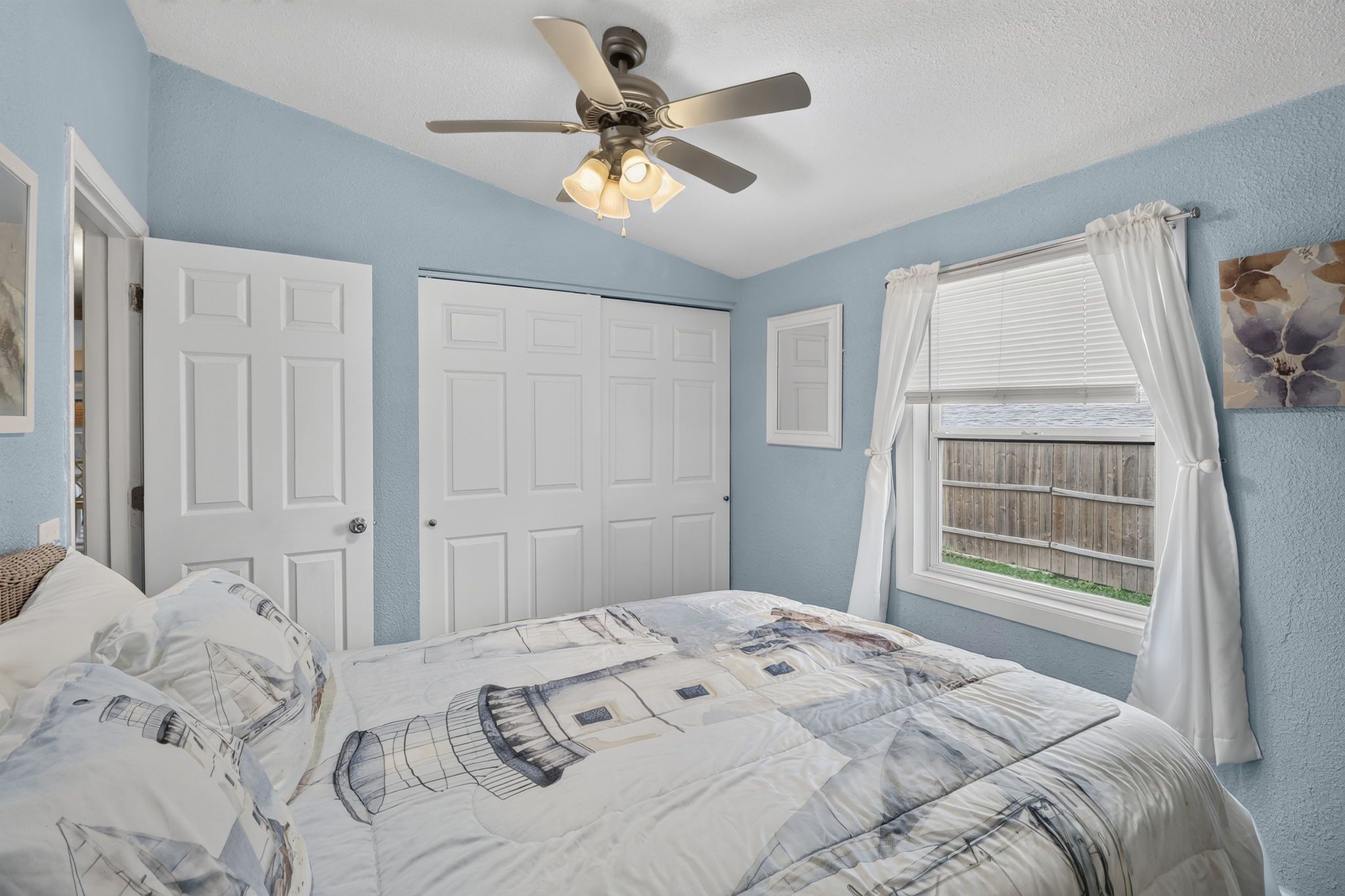 Un dormitorio con cama, ventilador de techo, ventana con cortinas y una puerta.
