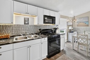 A modern kitchen with white cabinetry, a black stove, and a microwave. There is a sink with a stainless steel basin, and a decorative backsplash. - Modern 3‑Bedroom Lake House with Gorgeous Water & Wildlife Views (Toledo)