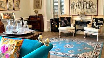 Une pièce avec un tapis bleu à motifs, deux fauteuils blancs, un canapé turquoise et un lustre.