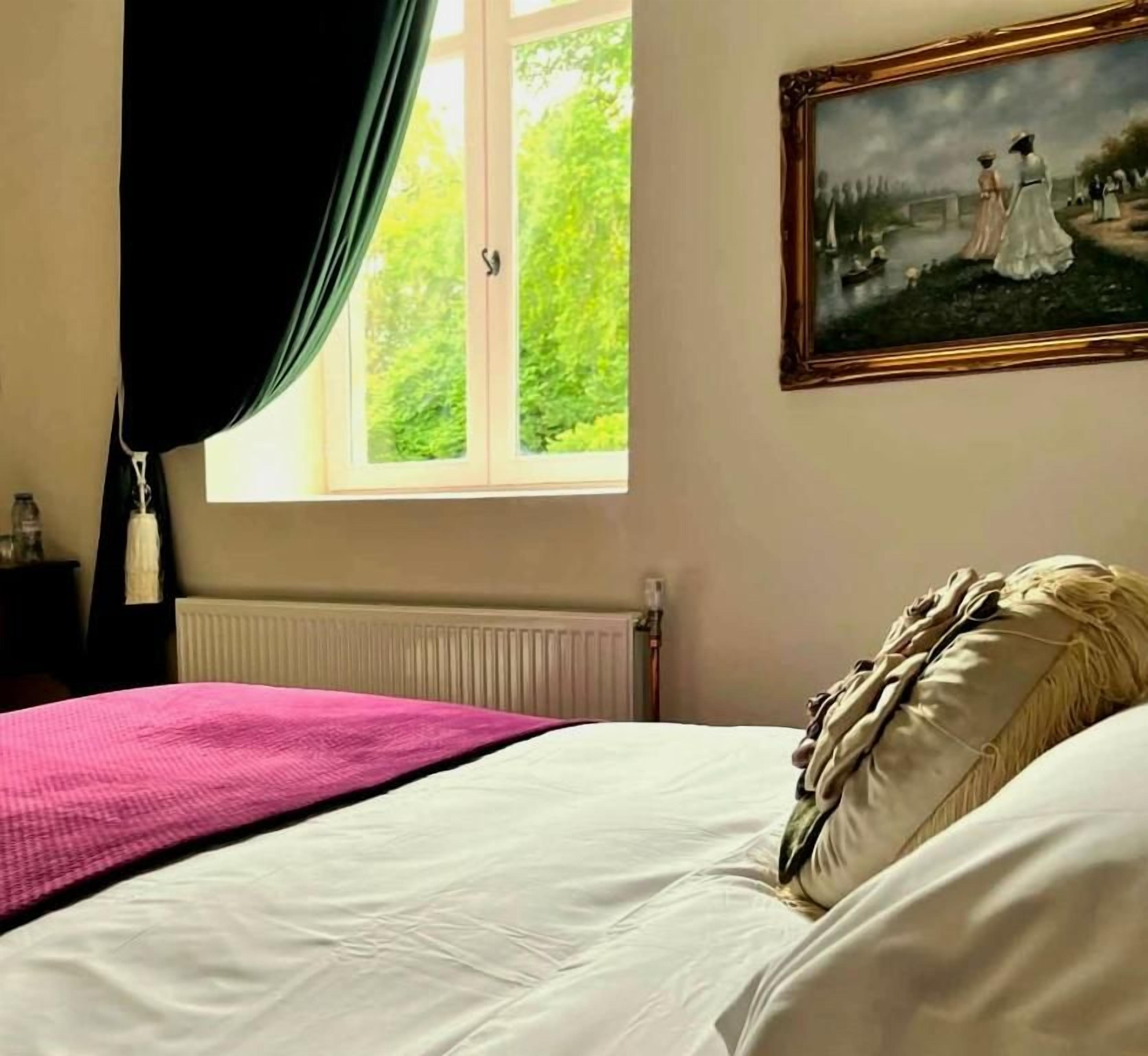 Une chambre à coucher avec un lit, une fenêtre avec des rideaux, un radiateur et un tableau accroché au mur.