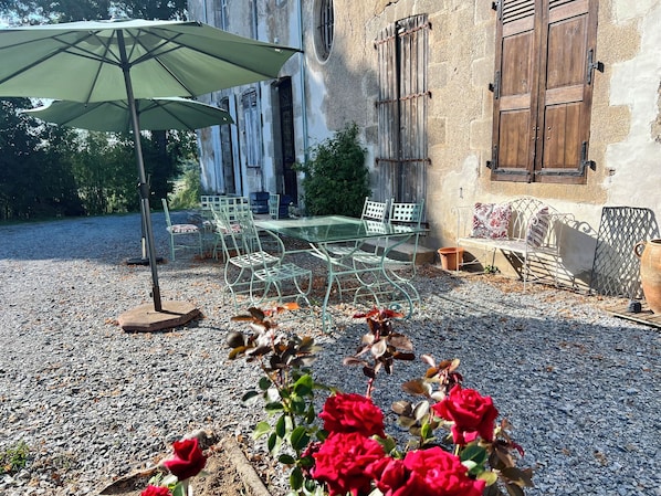 An outdoor patio with a table and chairs, a green umbrella, and red flowers.