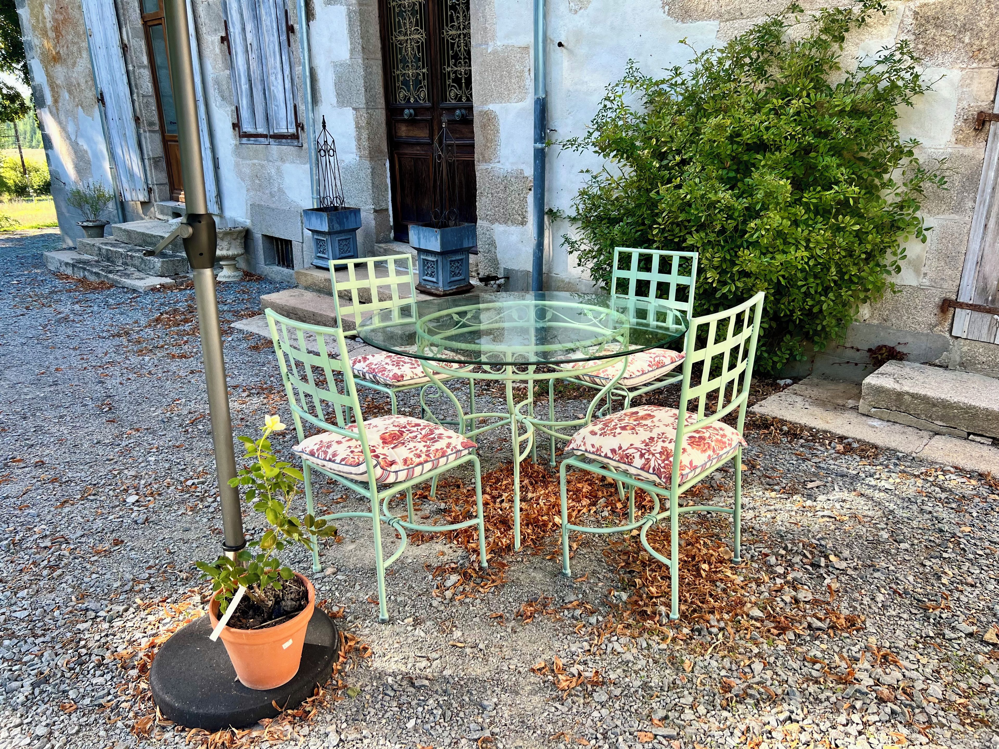 Een ronde glazen tafel met vier stoelen, een potplant en een stenen muur op de achtergrond.