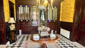 A room with a checkered floor, a round wooden table with books and a vase, a chandelier, and a large wooden door with glass panels.