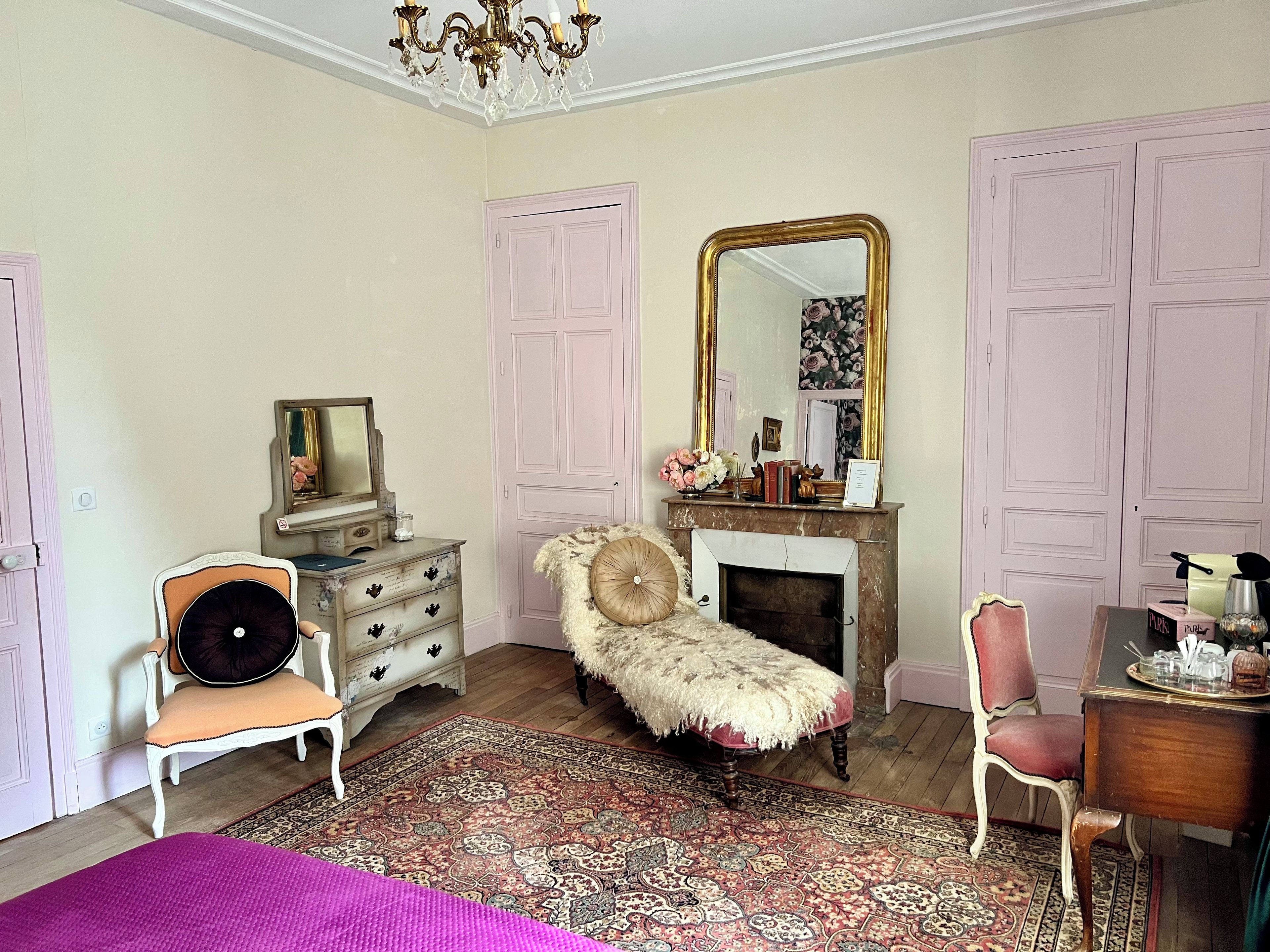 Une chambre à coucher avec une commode, une chaise, un miroir, une cheminée et un lit.