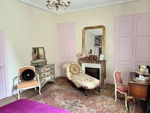 A bedroom with a dresser, a chair, a mirror, a fireplace, and a bed.