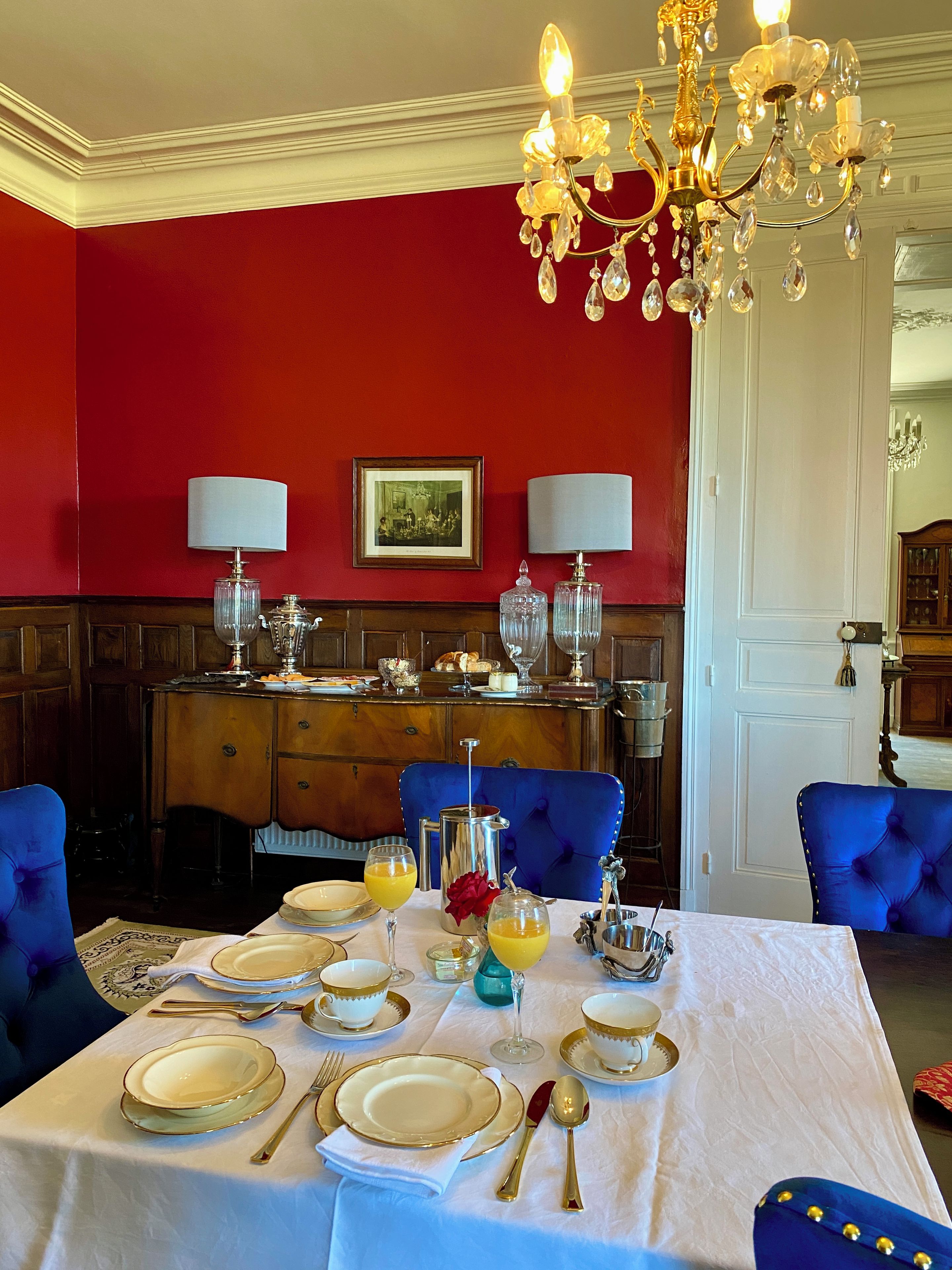 Comedor con pared roja, una araña y una mesa lista para una comida.