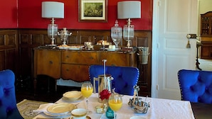 A dining room with a table set for four, featuring gold-rimmed plates, silverware, and crystal glasses.