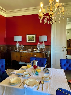 A dining room with a table set for four, featuring gold-rimmed plates, silverware, and crystal glasses.
