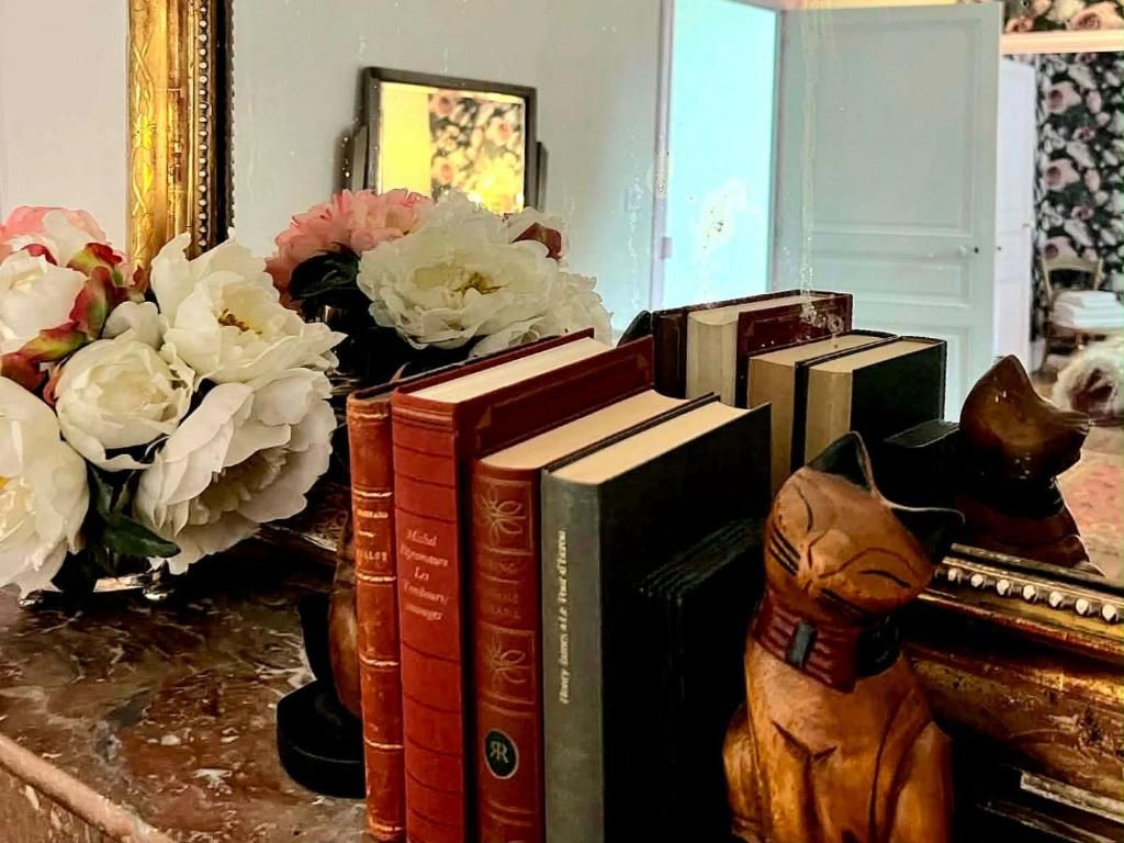A collection of books, a vase with flowers, and a small statue on a surface.