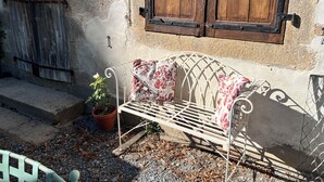 A metal bench with floral cushions, a potted plant, and a rustic wooden door.