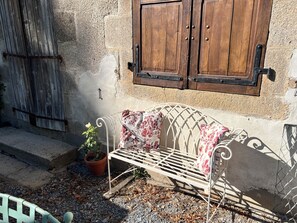 A metal bench with floral cushions, a potted plant, and a rustic wooden door.