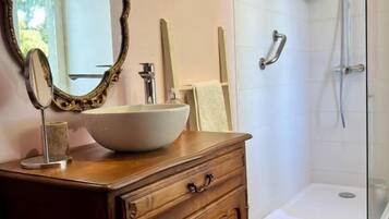 Een badkamer met een houten wastafelmeubel, een grote spiegel, een witte wasbak en een douchecabine met glazen wanden.