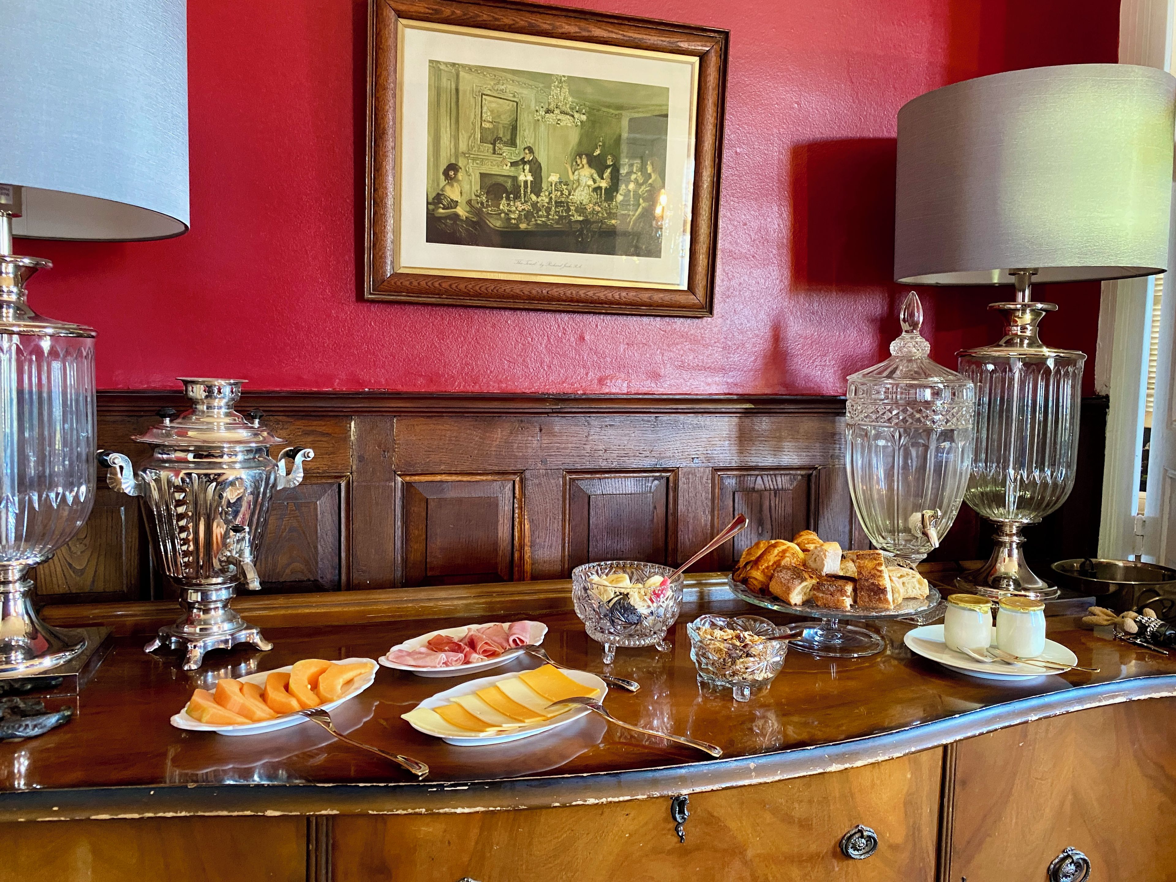 Een bar met een rode muur, een ingelijst kunstwerk en diverse etenswaren op het aanrecht.