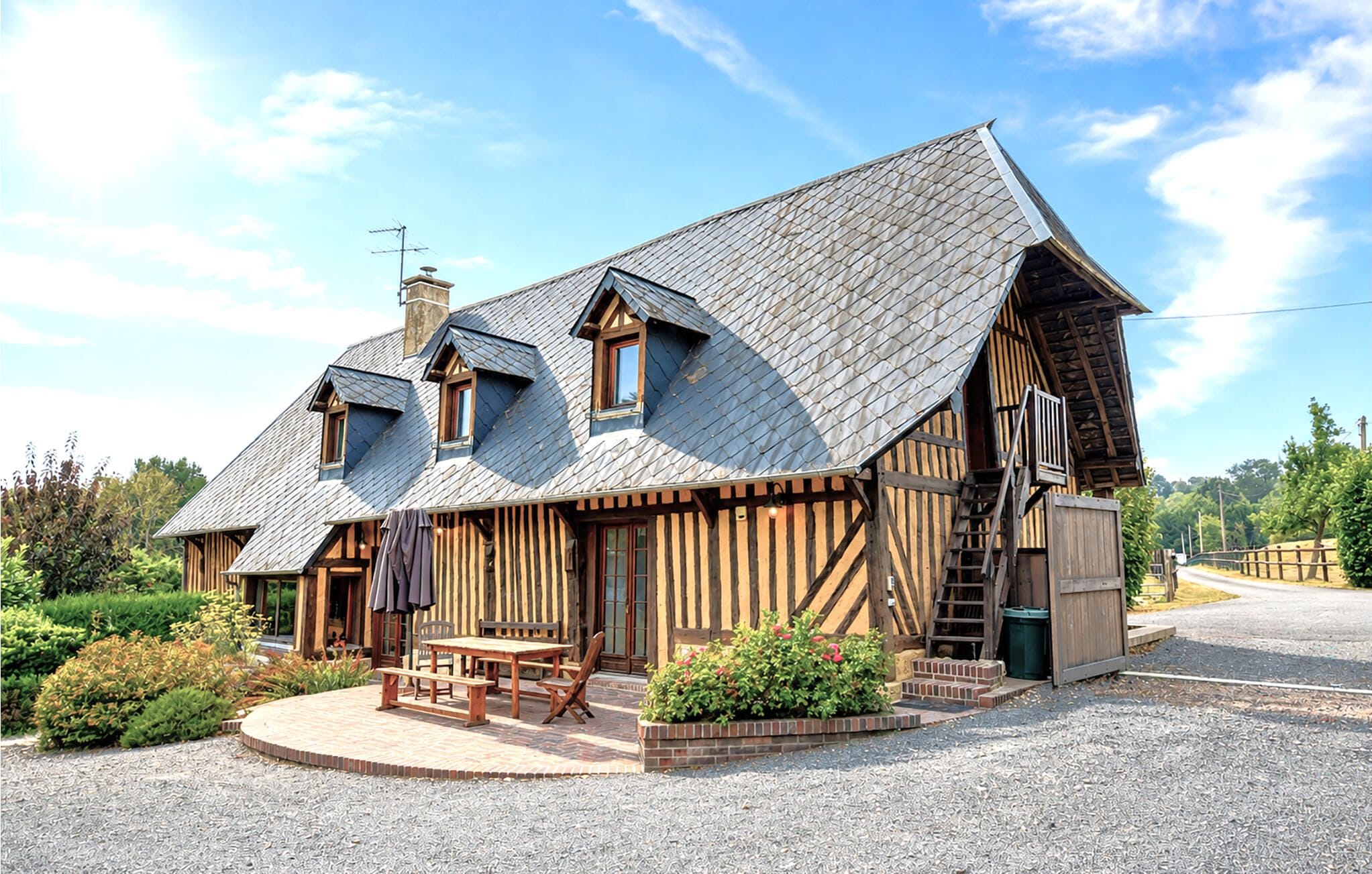 A traditional wooden house with a sloped roof, a wooden porch, and a gravel driveway.