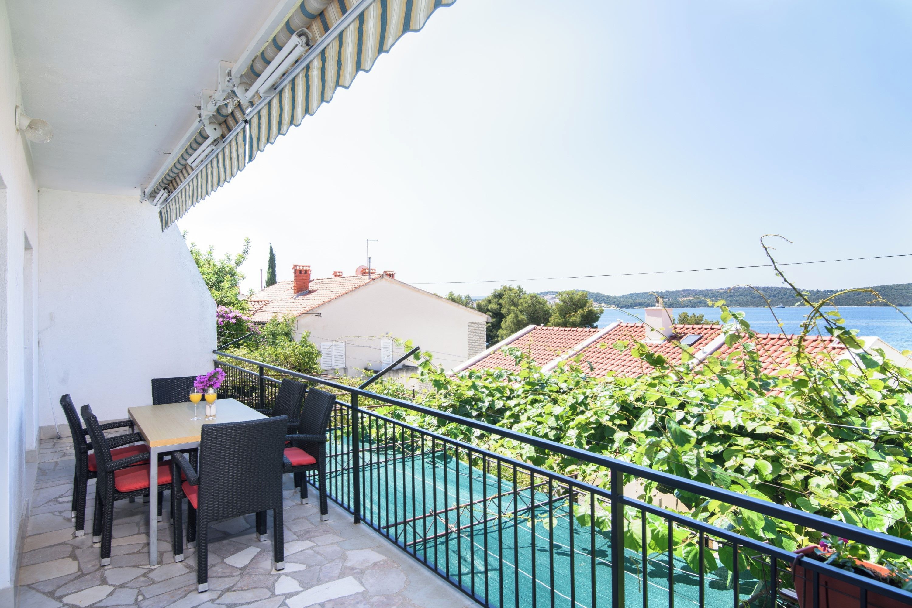 A balcony with outdoor furniture, a view of a swimming pool, and a distant view of a town and sea.