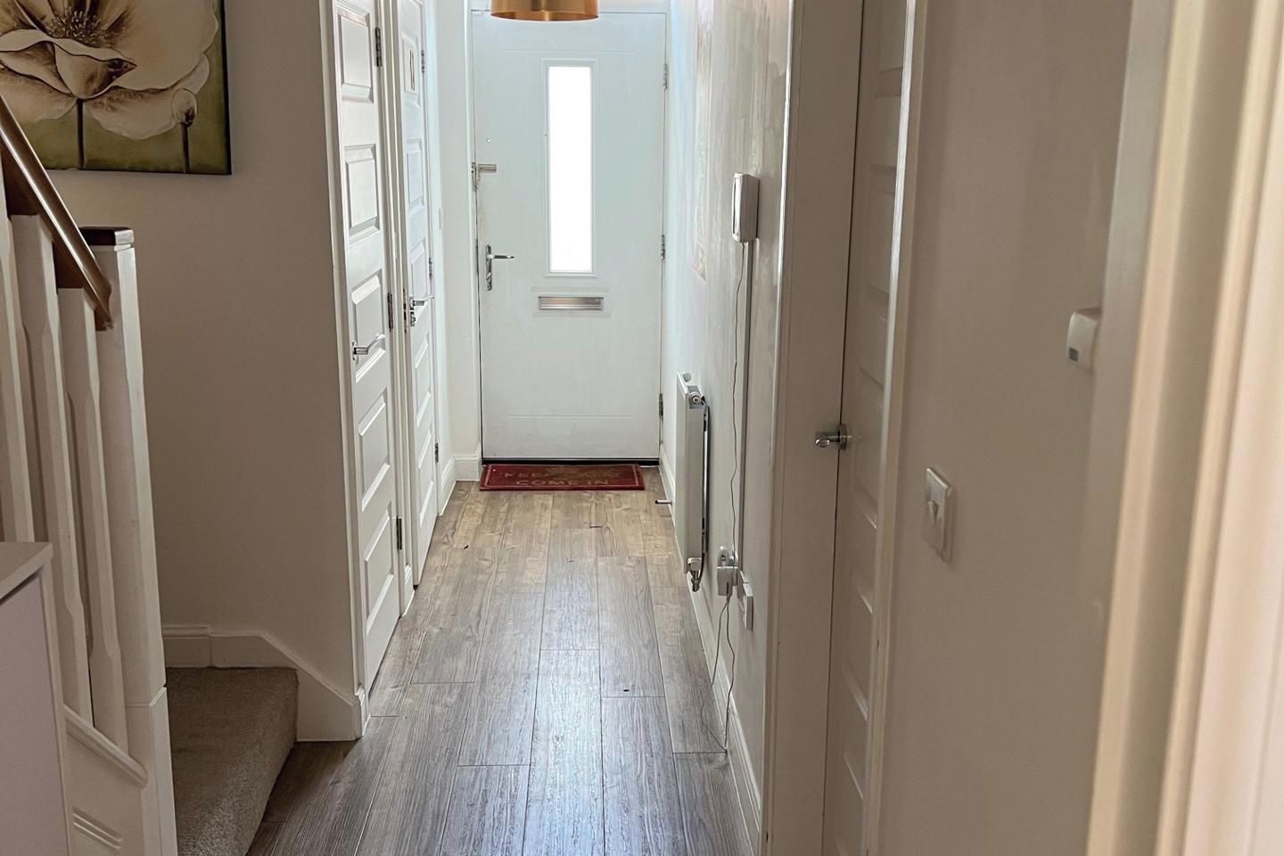 A narrow hallway with a wooden floor, white doors, and a radiator on the right.
