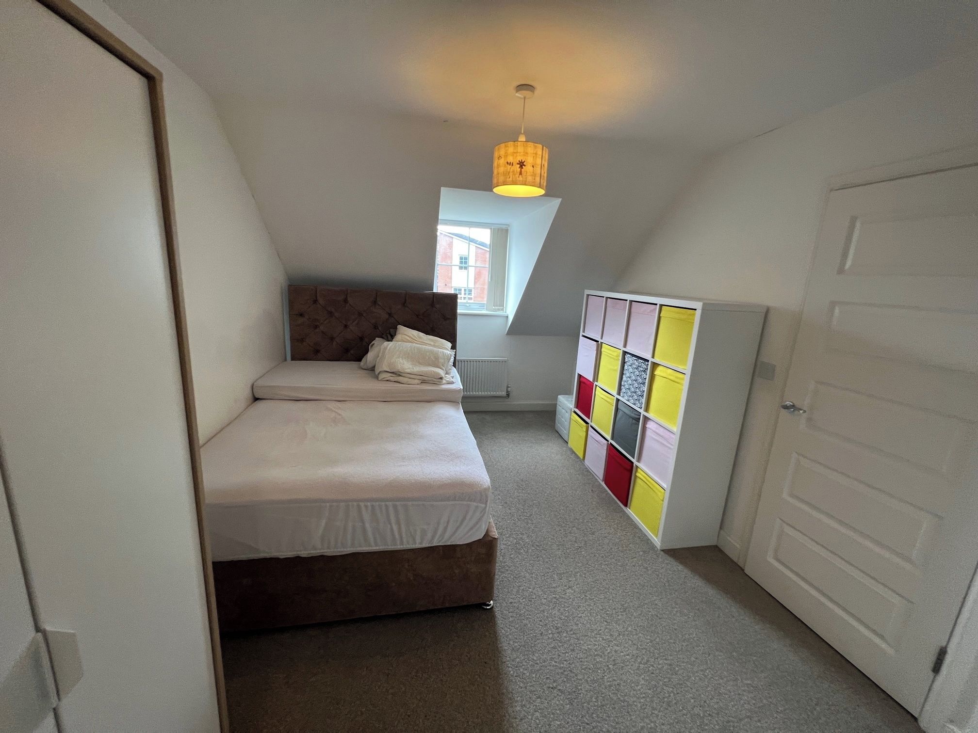 A bedroom with a bed, a wardrobe, a radiator, and a window.