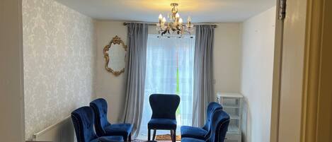 A room with a chandelier, a large mirror, two blue chairs, a radiator, and a window with curtains.