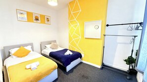 Ein Hotelzimmer mit zwei Betten, einer Wanduhr und einem Wäscheständer.